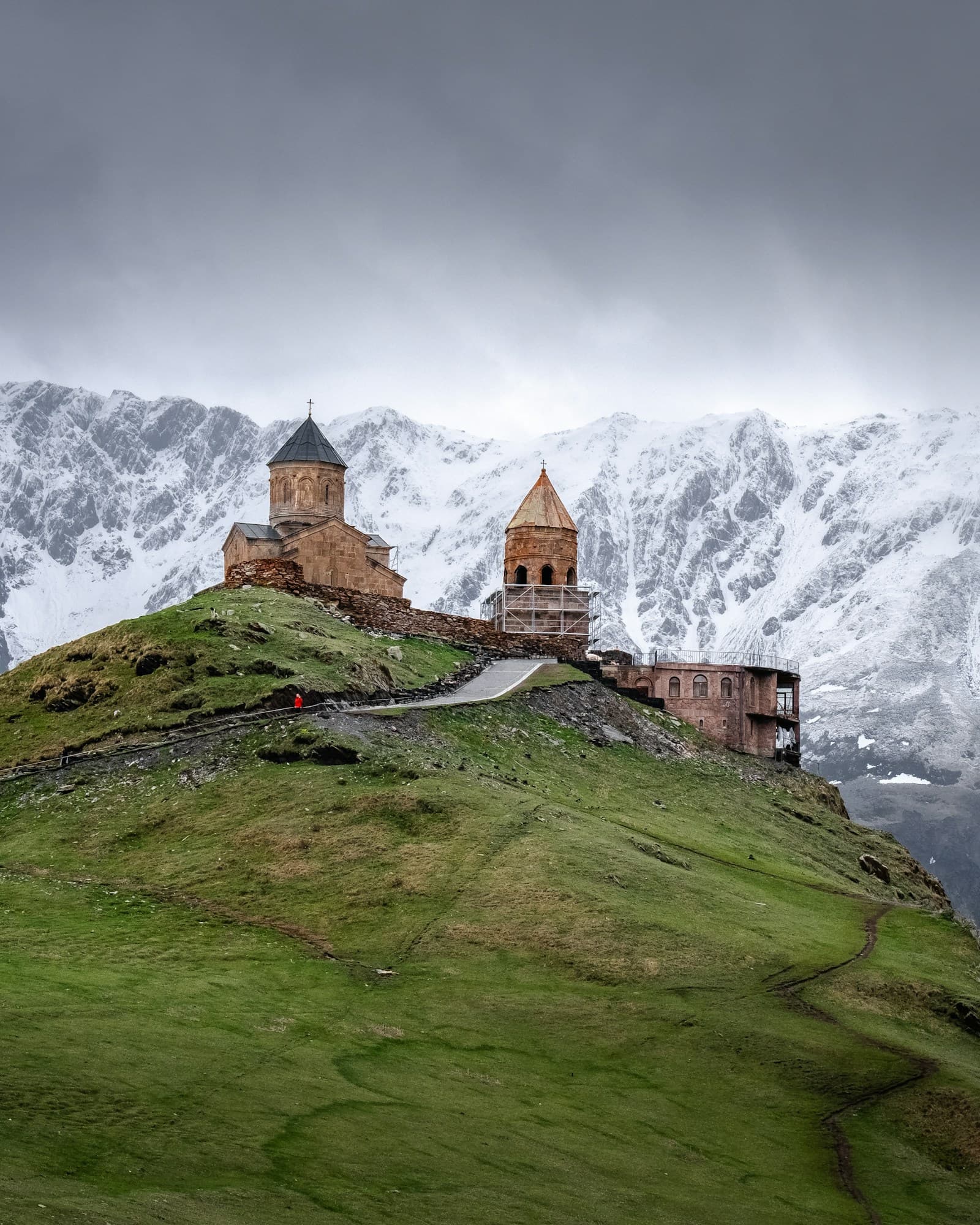 Gergeti Trinity Church on a green hillside beneath the snow-covered Caucasus Mountains in Georgia